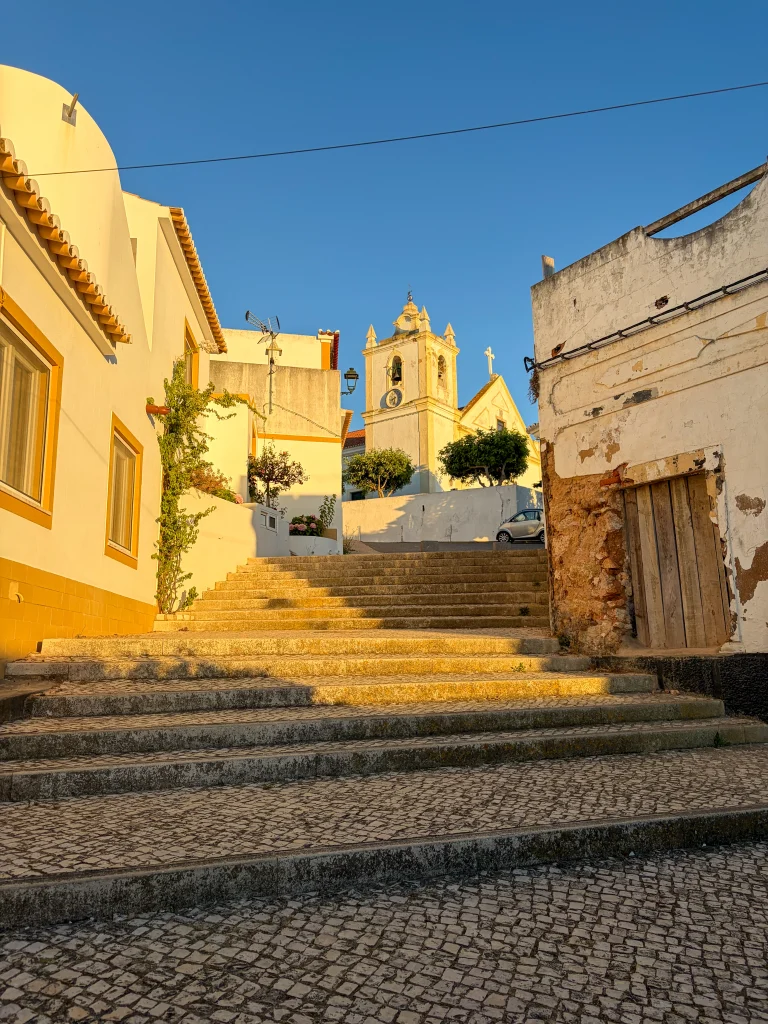 A quiet sunlit village street with stone steps and an old wooden door